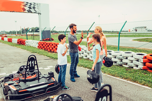 Family go-Karts together. They just finished their race on driveway and saluting with high-five.
