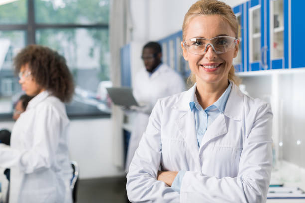 portrait de sourire femme en blouse blanche et lunettes de protection en laboratoire moderne, femme scientifique au cours de l’équipe de chercheurs occupé - medical exam science research scientific experiment photos et images de collection