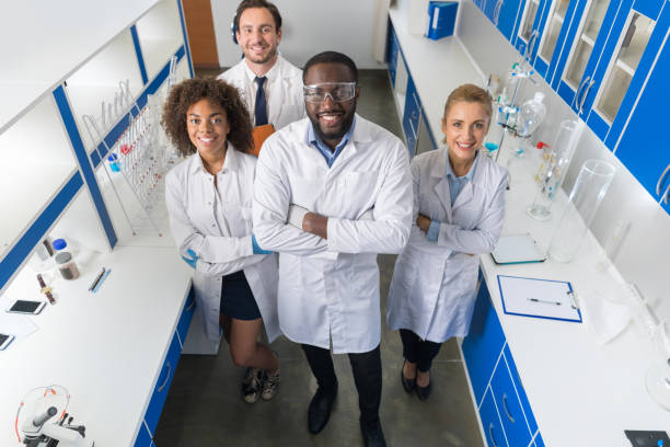 afrikanische amerikanischer wissenschaftler mit gruppe von forschern in modernen labor glücklich lächelnd, mischen rennteam der wissenschaftler im labor - healthcare and medicine smiling group of people lab coat stock-fotos und bilder