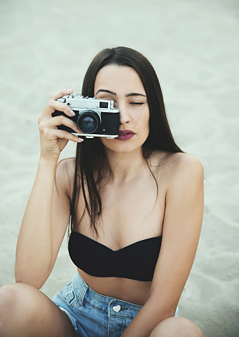 Hipster girl with retro camera taking photos on beach