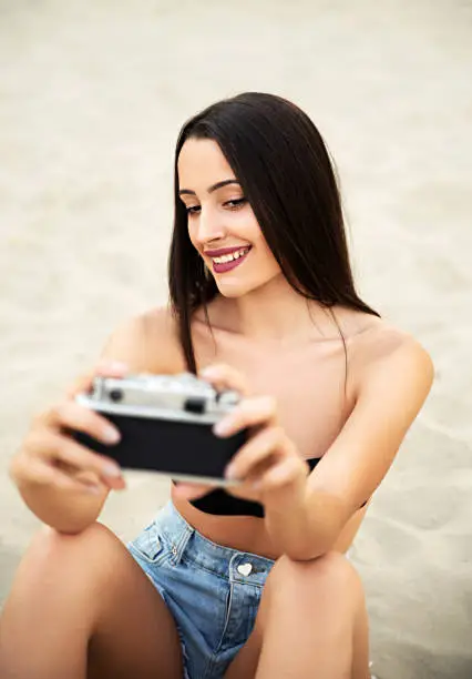 Hipster girl taking selfie on beach with vintage camera