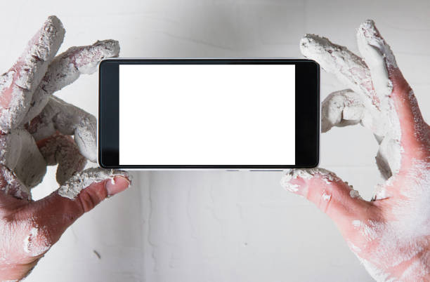 Worker hands in white plaster with smartphone take photo of stucco wall, flat lay. Unrecognizable person with empty screen phone, pov.