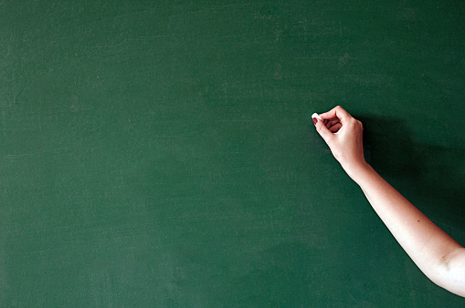 Close up of hand holding chalk on blank chalkboard. Blank blackboard / chalkboard. Hand writing on green chalk board holding chalk. Great texture for text.