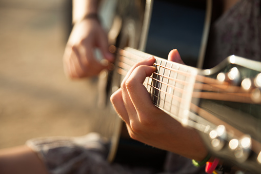 Teen girl playing acoustic guitar, detail, shallow DOF.