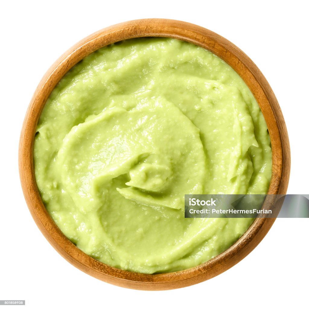 Avocado cream in wooden bowl over white Avocado cream in wooden bowl. Alligator pear, the fruit of the Persea americana tree. Light green paste of mashed avocados and lemon juice. Macro food photo close up from above on white background. Avocado Stock Photo