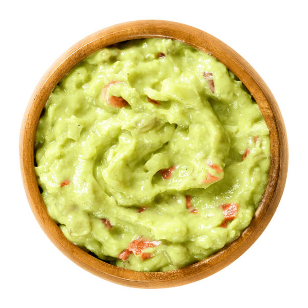 Guacamole, avocado dip, in wooden bowl Guacamole in wooden bowl. Also short guac, a light green dip or salad, made of mashed avocados, tomatoes, onions, garlic, lemon, cayenne pepper and salt. Macro food photo close up on white background. guacamole photos stock pictures, royalty-free photos & images