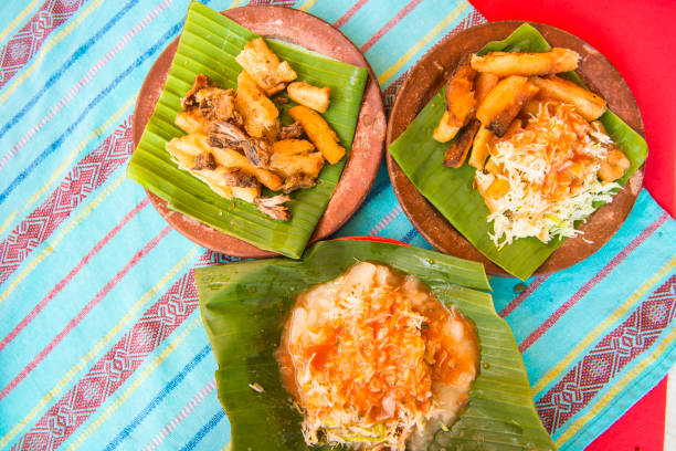 Three servings of Fried Yucca Sticks with meat and cabbage on palm leaf on plate. View directly above on turquoise table cloth. El Salvador traditional meal.