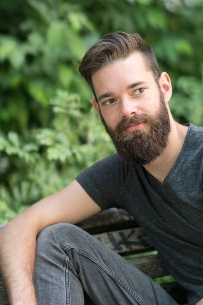 istock Thoughtful bearded guy sitting on a bench in park 801936824