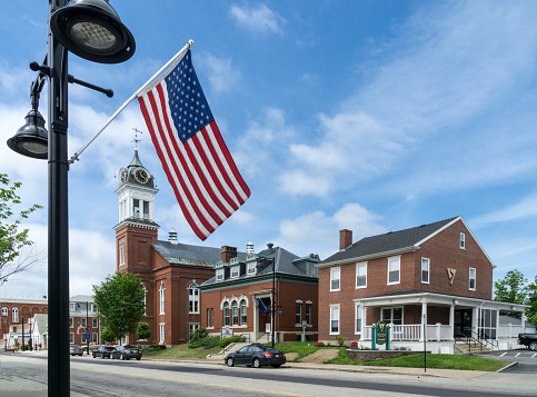 Saco, Maine, USA — May 28, 2017: An American flag flies over the historic Main Street in downtown Saco, Maine. The Town Hall is at left.