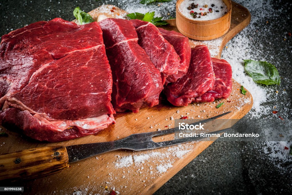 Meat. Beef, veal. Fresh raw tenderloin Meat. Beef, veal. Fresh raw tenderloin, piece without bone. For frying grilling barbecue. Cut into steaks, whole. On black stone table,cutting board, spices, salt, fork for meat. Top view copy space Veal Stock Photo