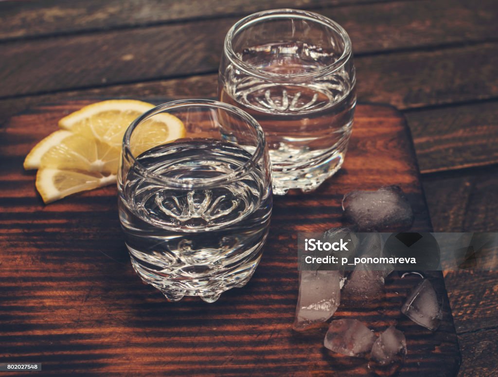 Gin tonic, vodka or rum with ice and lemon on wooden table. Retro styled background. Vodka Stock Photo