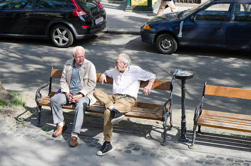 Two old men sitting in public bench and talking together in Budapest during summer day