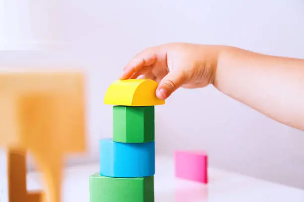 Baby playing and discovery with colorful toys at home, close-up detail. Toddler plays with toy blocks and constructors. Early development, learning and education of child or baby - background concept.