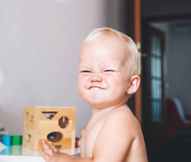 Cute toddler frowns and expresses disagreement on his face. Cute toddler frowns and expresses disagreement on his face. Adorable baby boy makes a funny serious disagrees displeased face at home interiors. Portrait of an angry child. Early development of baby protruding stock pictures, royalty-free photos & images