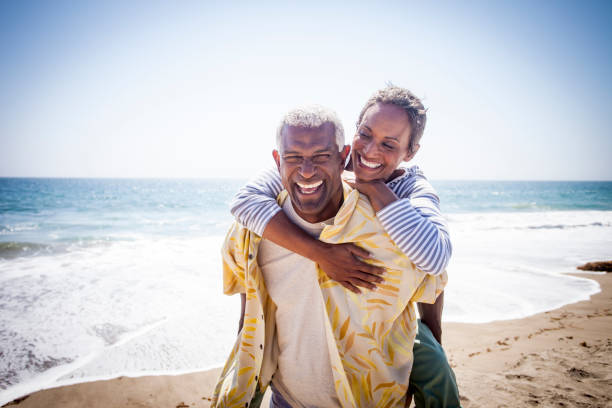 Black Couple Piggyback on Beach A beautiful senior black couple piggyback on the beach toothy smile photos stock pictures, royalty-free photos & images