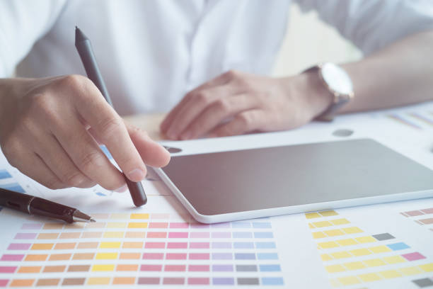 istock young graphic designer working with color swatch. creative man using stylus pen and digital tablet at modern office.  Architect drawing with work tools and sample colour catalog. business, technology, design and people concept 802124620