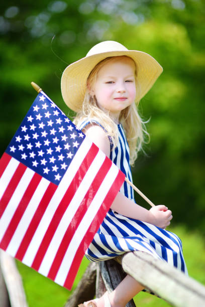 adorable little girl wearing hat holding american flag outdoors on beautiful summer day - child flag fourth of july little girls imagens e fotografias de stock