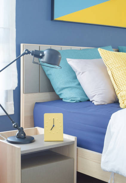 istock Yellow modern clock on bedside table with colorful pillows in background 802222754
