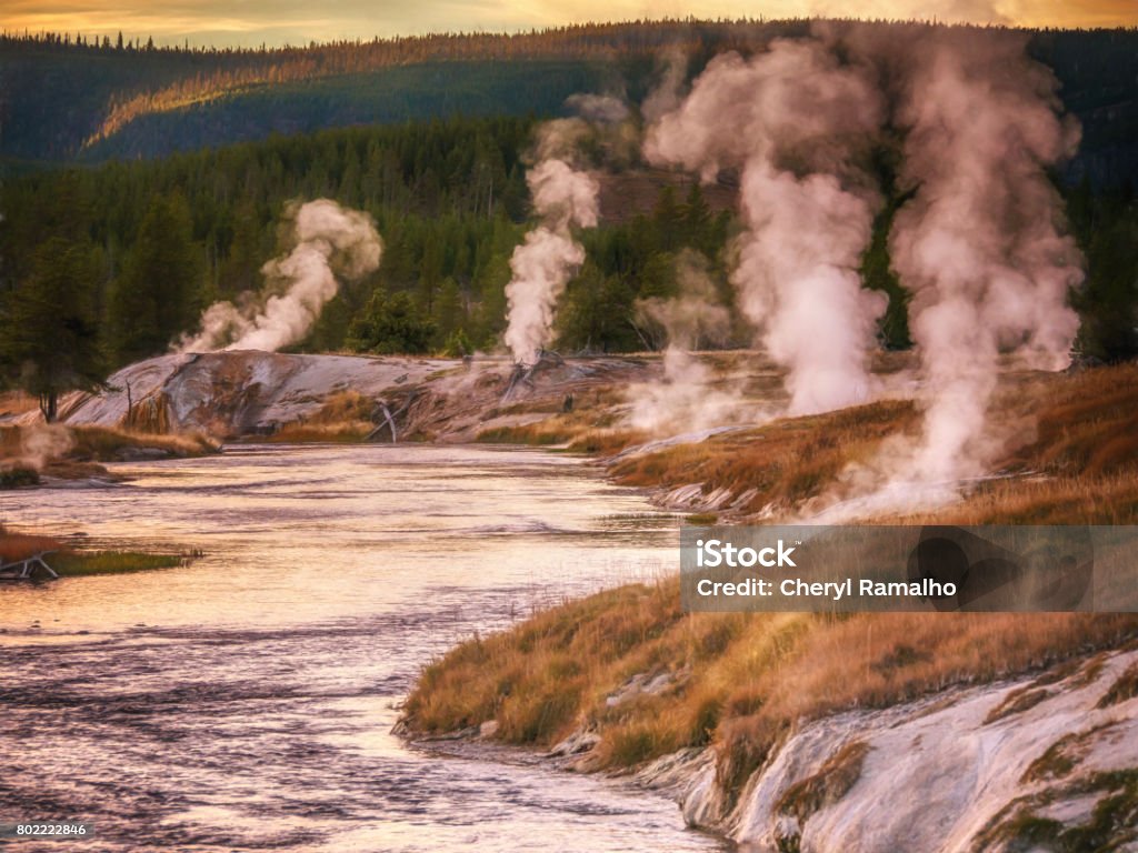 Thermal hot springs and geyser basin along the Firehole River, Yellowstone National Park, Wyoming, USA. Geothermal steam rising beside the riverbank at dusk in late summer, early autumn. Autumn Stock Photo