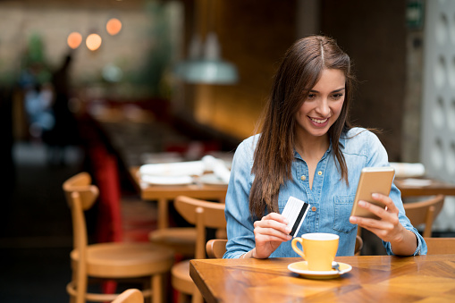 Portrait of a happy young woman at a cafe shopping online on her cell phone - lifestyle concepts