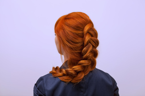 Beautiful girl with long red hair, braided with a French braid, in a beauty salon. Professional hair care and creating hairstyles.