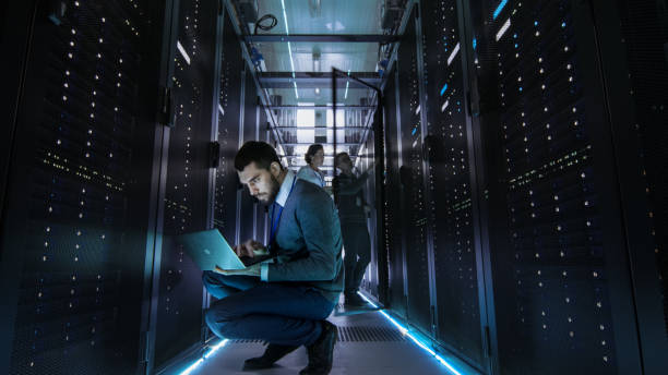 istock IT Technician Works on Laptop in Big Data Center full of Rack Servers. Multiple People Works at Data Center at the same time. 802301222
