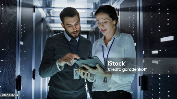 Male And Female It Engineers In Data Center Server Room They Are Talking One Of Them Holds Tablet Computer Stock Photo - Download Image Now