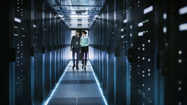 female it technician and male server engineer talk and discuss. they are in working data center full of rack servers. woman holds laptop. - network server rack computer mainframe imagens e fotografias de stock