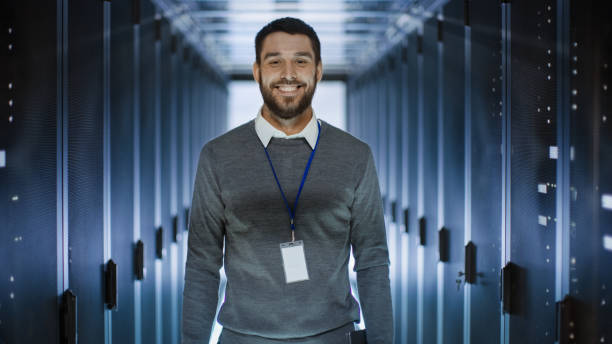 portrait of an it engineer, he smiles and folds his arms on a chest. he's working in data center full of rack servers. - network server rack data center in a row imagens e fotografias de stock