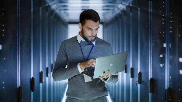 ingénieur mâle server fonctionne sur un ordinateur portable dans le grand centre de données. - network server data center installing photos et images de collection