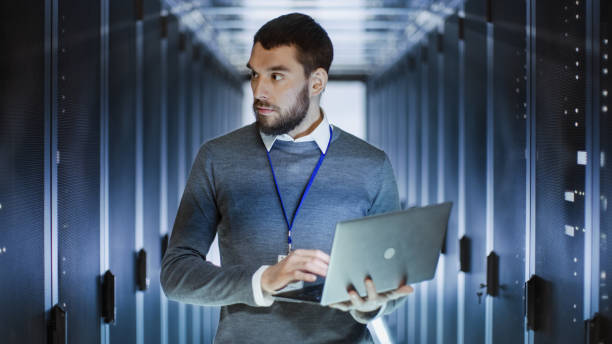 istock Male IT Specialist Holds Laptop and Discusses Work with Female Server Technician. They're Standing in Data Center, Rack Server Cabinet is Open. 802301392