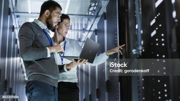 Male It Specialist Holds Laptop And Discusses Work With Female Server Technician Theyre Standing In Data Center Rack Server Cabinet Is Open Stock Photo - Download Image Now