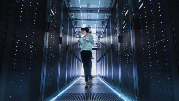 istock Female IT Engineer Walking through Data Center Corridor. She is Holding Tablet Computer. She is Blurred in Motion. 802301416