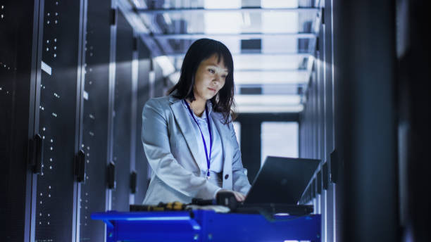 ingegnere it femminile asiatico che lavora su un laptop su carrello utensili, esegue la scansione dei dischi rigidi.  è in un big data center pieno di server rack. - computer network server repairing technology foto e immagini stock