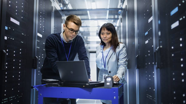 istock Caucasian Male and Asian Female IT Technicians Working with Computer Crash Cart in Big Data Center full of Rack Servers. 802301522