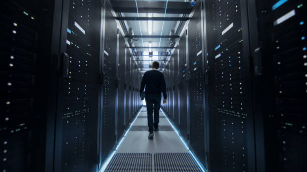 istock Following Shot of IT Engineer Walking Through Data Center Corridor with Rows of Rack Servers. 802303640