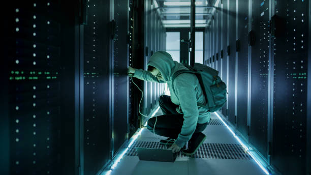 a hooded hacker with laptop connects to rack server and steals information from corporate data center. - network server rack data center in a row imagens e fotografias de stock