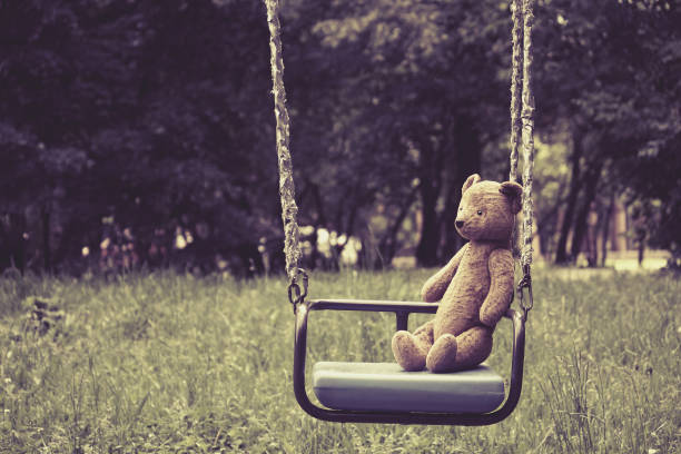 Old toy teddy bear sitting on swing in park