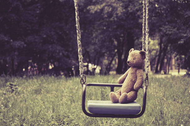 Old toy teddy bear sitting on swing in park Old toy teddy bear sitting on swing in park, retro style, toned effect behavior teddy bear doll old stock pictures, royalty-free photos & images