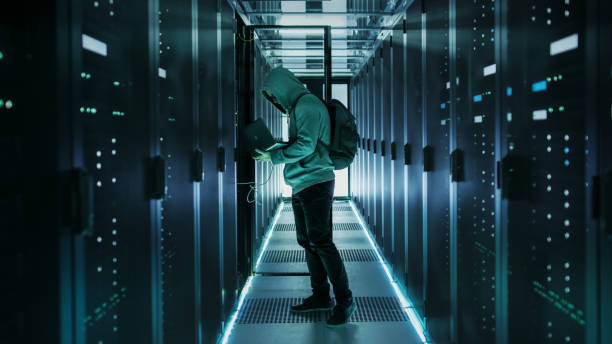 a hooded hacker with laptop connects to rack server and steals information from corporate data center. - network server rack data center in a row imagens e fotografias de stock