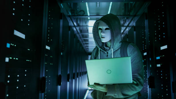 Close-up Shot of a Masked Hacker in a Hoodie Standing in the Middle of Data Center full of Rack Servers and Hacking it with His Laptop. Close-up Shot of a Masked Hacker in a Hoodie Standing in the Middle of Data Center full of Rack Servers and Hacking it with His Laptop. air attack photos stock pictures, royalty-free photos & images