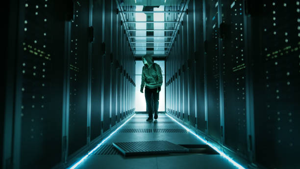 istock Hooded Hacker in a Mask Walks Through Working Data Center with Open Floor Hatch in the Middle of it. 802320772