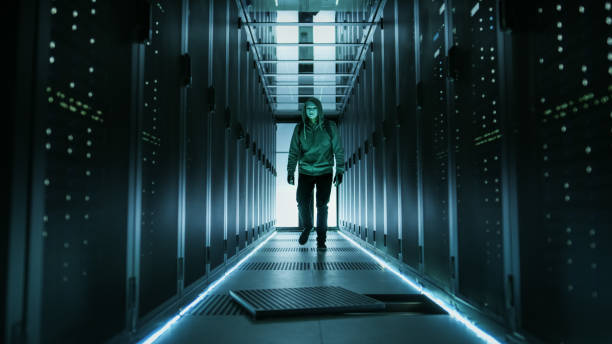 istock Hooded Hacker in a Mask Walks Through Working Data Center with Open Floor Hatch in the Middle of it. 802320790
