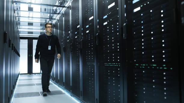istock IT Engineer Holding Notebook and Walking Through Data Center Full of Working Rack Servers. 802320826