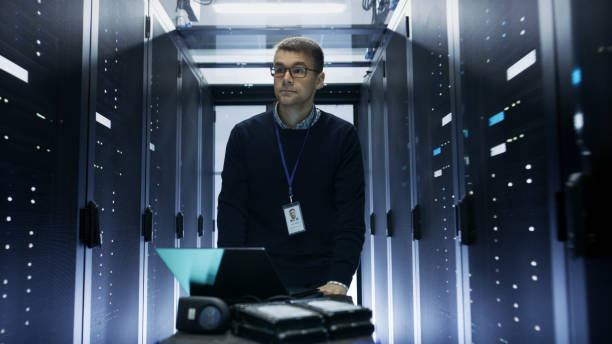 istock Shot of Server Engineer Pushing Crash Cart with Laptop, Hard Drives and Hardware Through Data Center. He Walks along Rows of Server Racks. 802320856