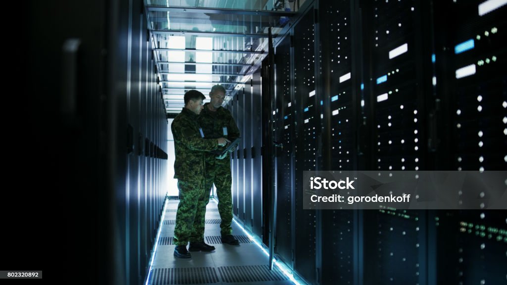 In Data Center Two Military Men Work with Open Server Rack Cabinet. One Holds Military Edition Laptop. Military Stock Photo