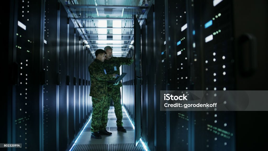 데이터 센터에서 두 군사 남자 오픈 서버 랙 캐비닛 작동. 하나는 군사 에디션 노트북을 보유 하고있다. - 로열티 프리 군사 스톡 사진