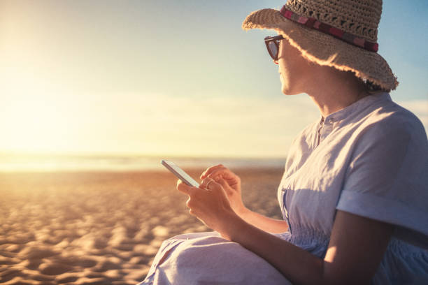 istock Young woman using smart phone sitting on the beach 802331198