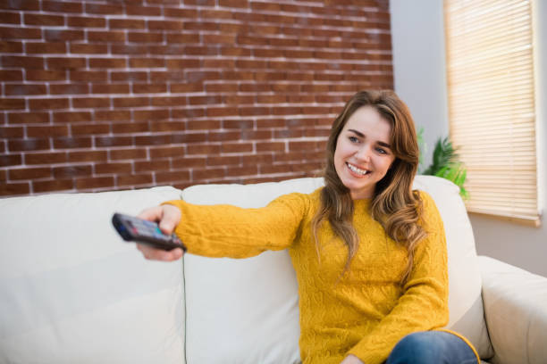 istock Smiling woman holding remote control on couch 802334072