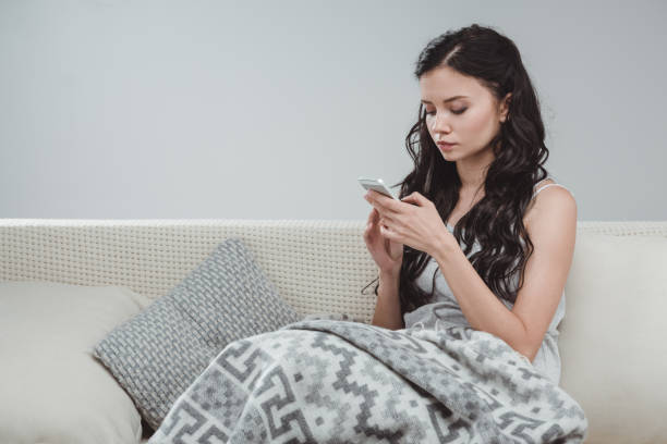istock Beautiful young woman using smartphone while sitting on sofa at home 802337370
